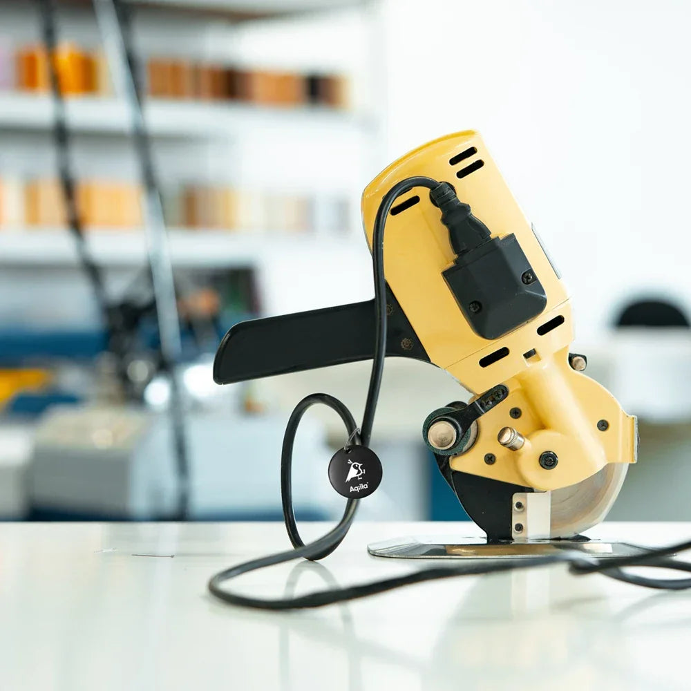 Gul elektrisk kappsag med kabel på arbeidsbord, verkstedutstyr i bakgrunnen