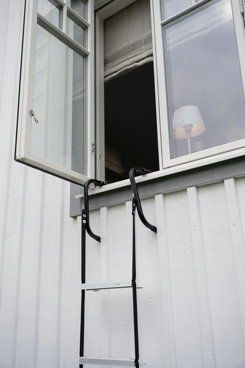 Brannstige for evakuering montert i et åpent vindu på hvit husvegg