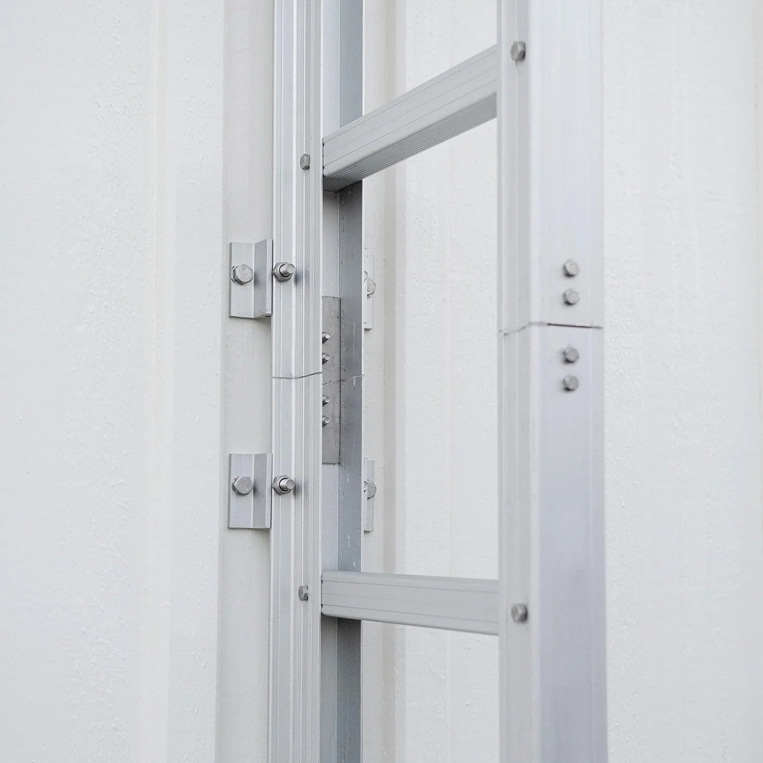 Fastmontert rømningsstige i aluminium på hvit vegg, for brannsikkerhet og evakuering.