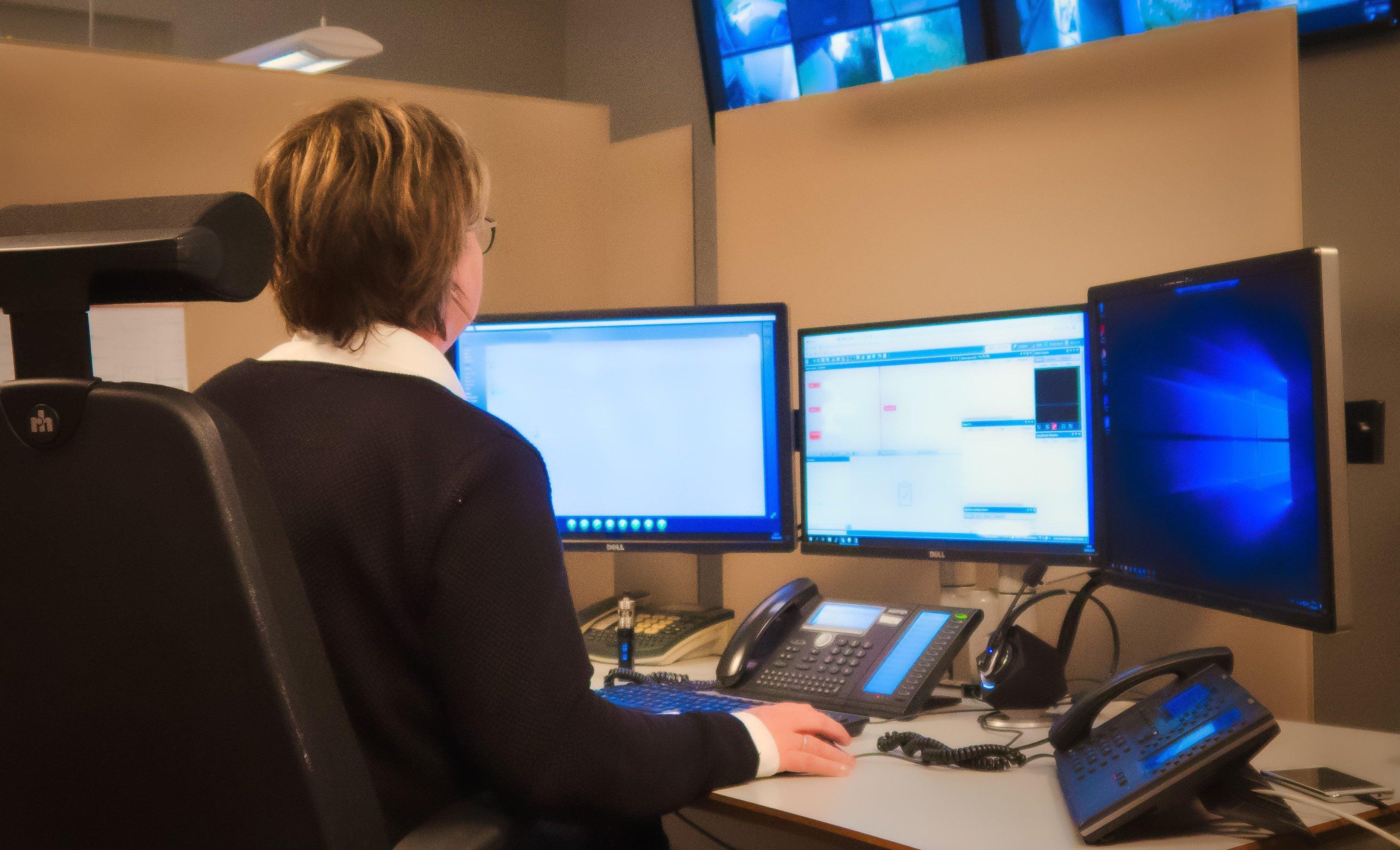 Ansatt på vaktsentral foran flere skjermer, overvåking og sikkerhet i kontrollrom