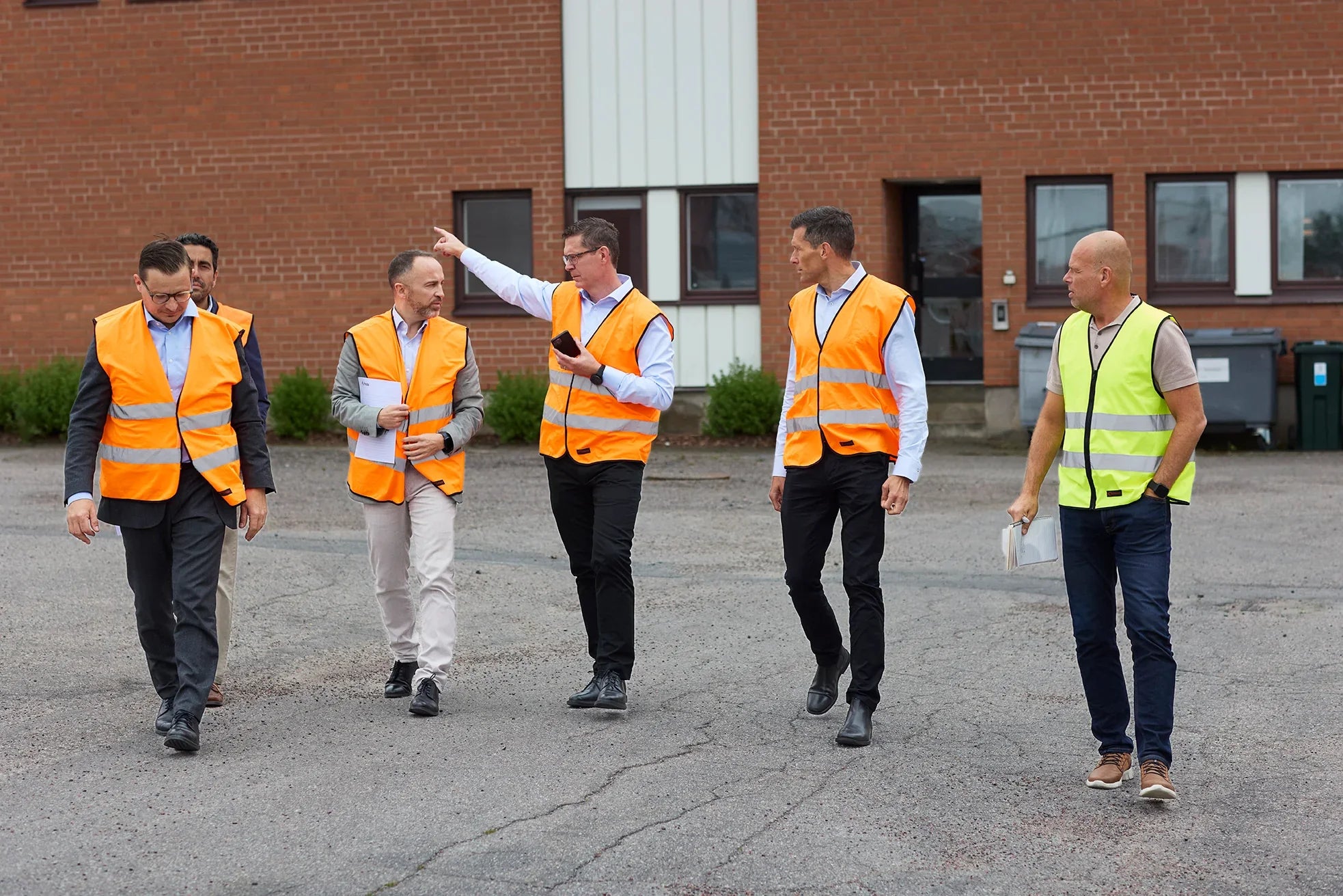 Fem menn med refleksvester i samtale utenfor en bygning, sikkerhetsinspeksjon.