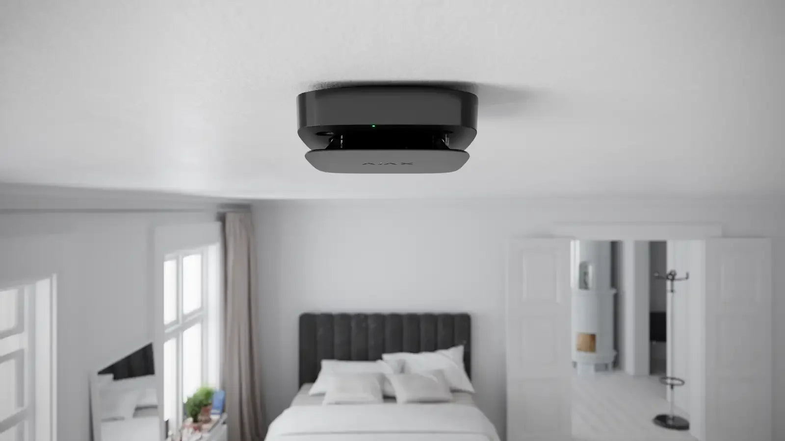 Moderne sort røykvarsler montert i taket på et lyst soverom med seng og vinduer