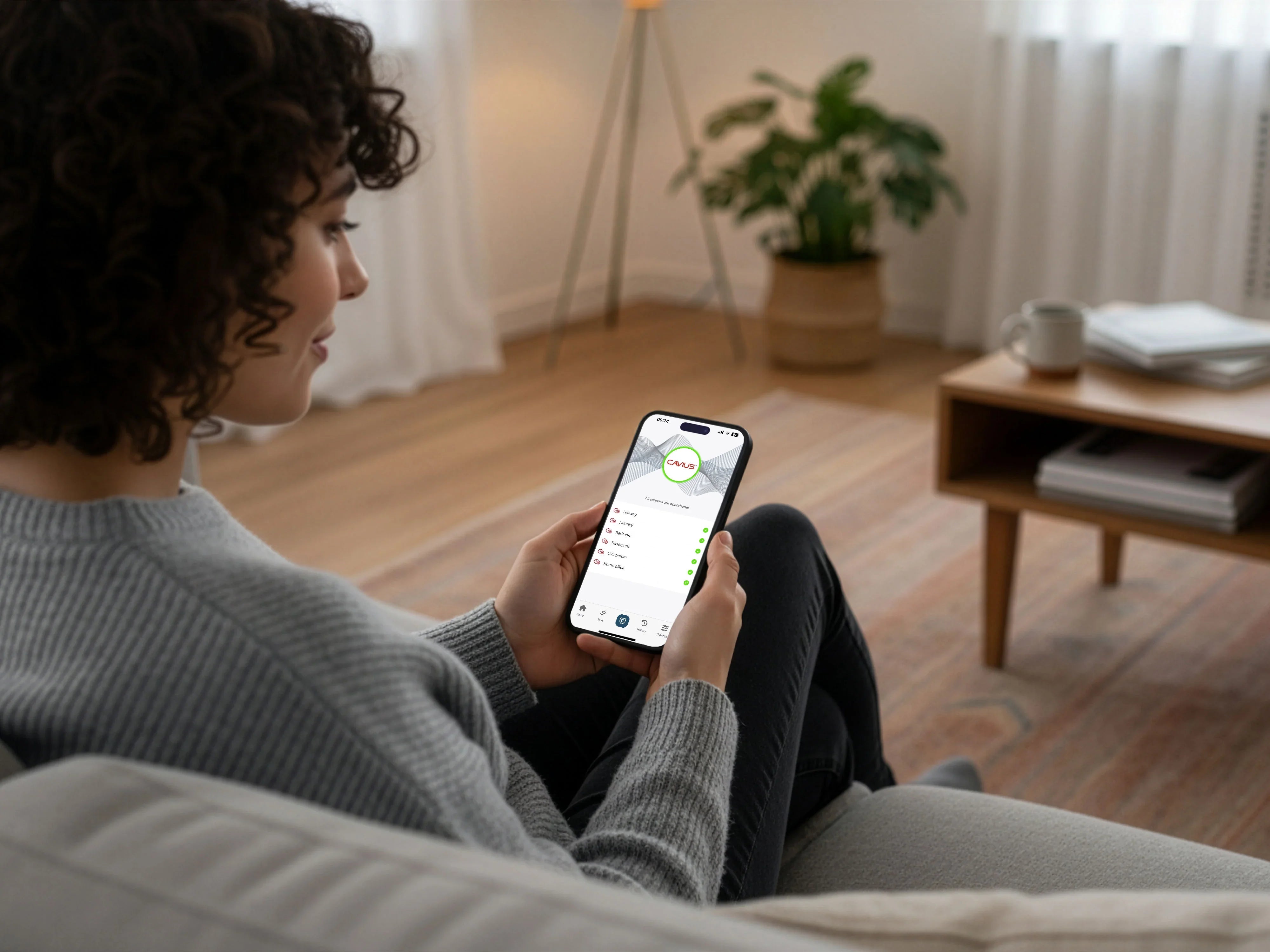 Kvinne styrer brann- og sikkerhetssystem via mobilapp i moderne stue med planter.
