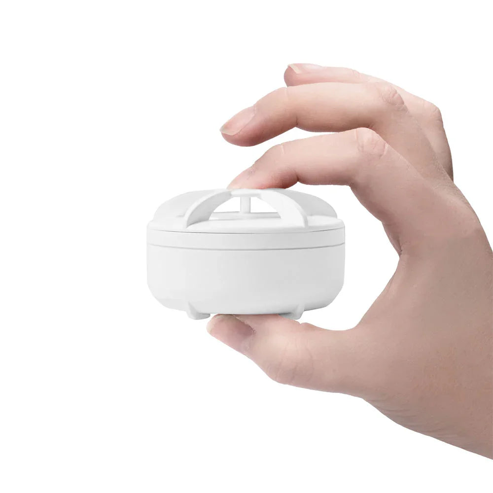 Hånd holder kompakt, hvit flomsensor for vannlekkasjealarm på hvit bakgrunn