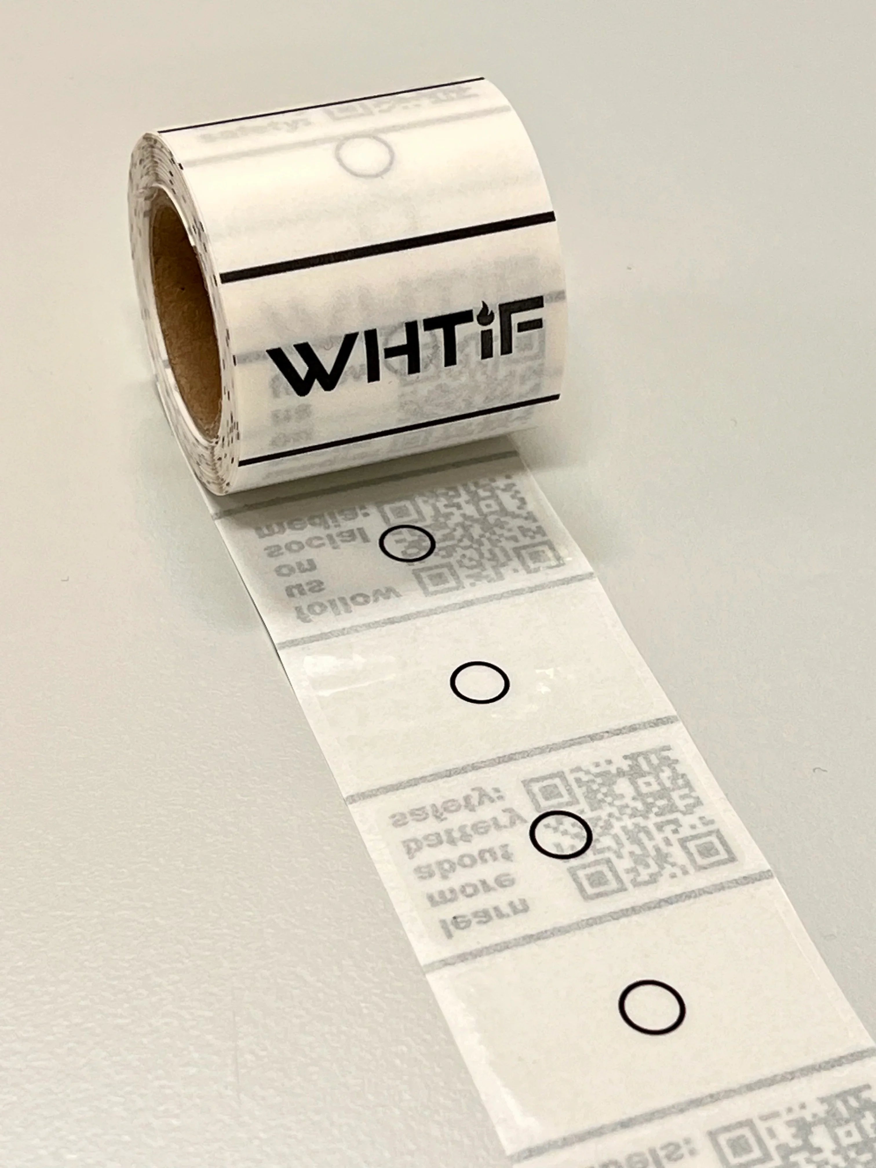 Rull med selvklebende etiketter med sirkler og QR-koder, liggende på bord