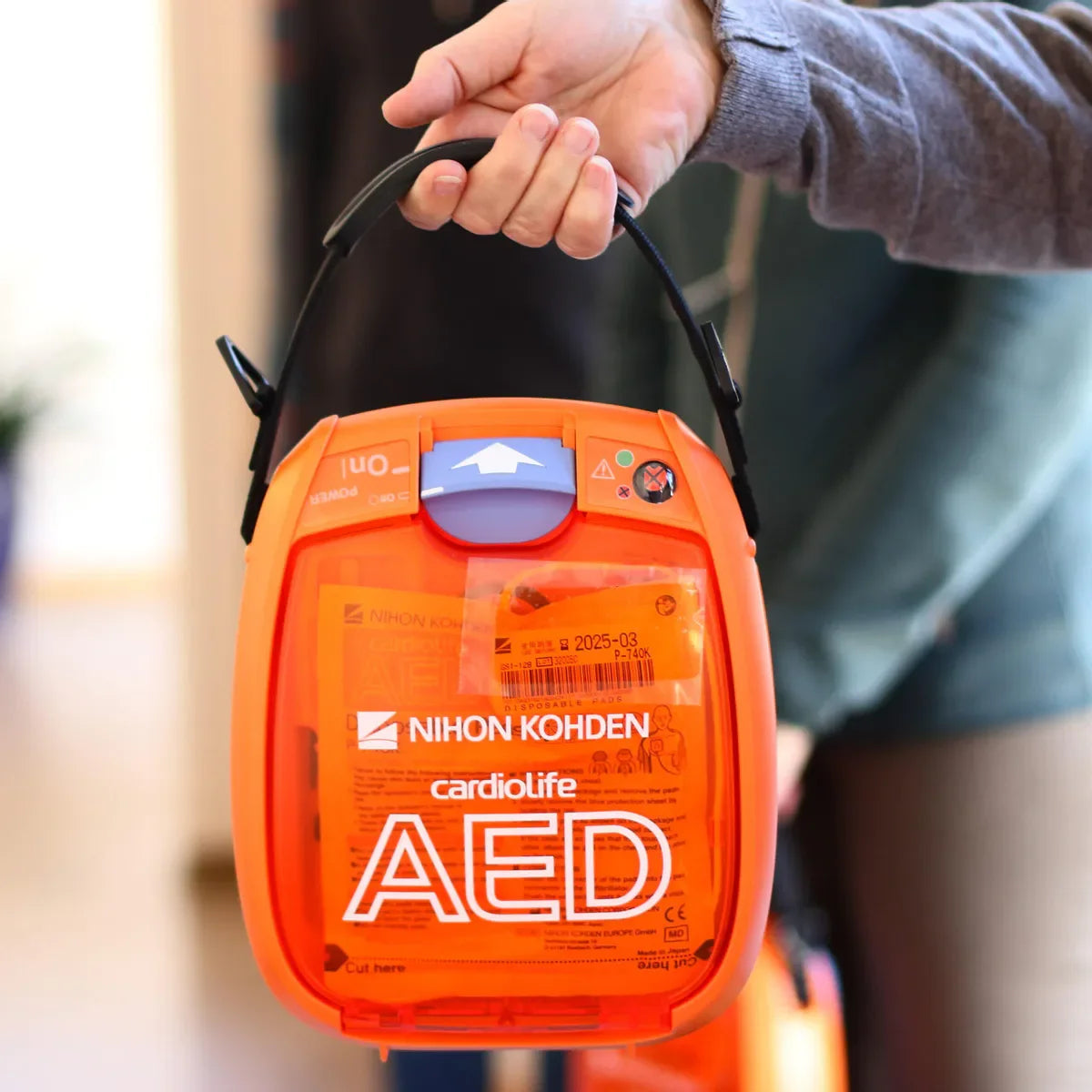 Person holder bærbar hjertestarter AED fra Nihon Kohden, førstehjelpsutstyr innendørs