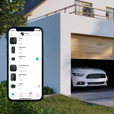 Smarttelefon viser sikkerhetsapp foran moderne hus med åpen garasje og bil parkert inne.