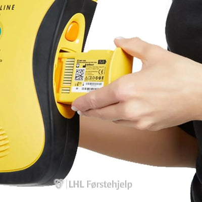 Hånd setter inn batteri i gul hjertestarter, førstehjelpsutstyr for gjenoppliving.